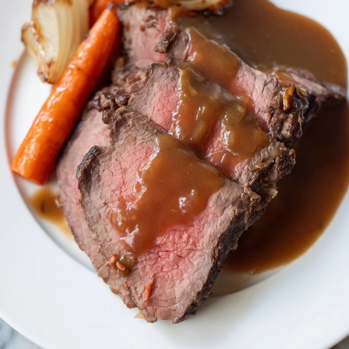 Perfectly roasted beef with gravy, sliced to reveal a juicy pink center, served with roasted carrots and onions. 