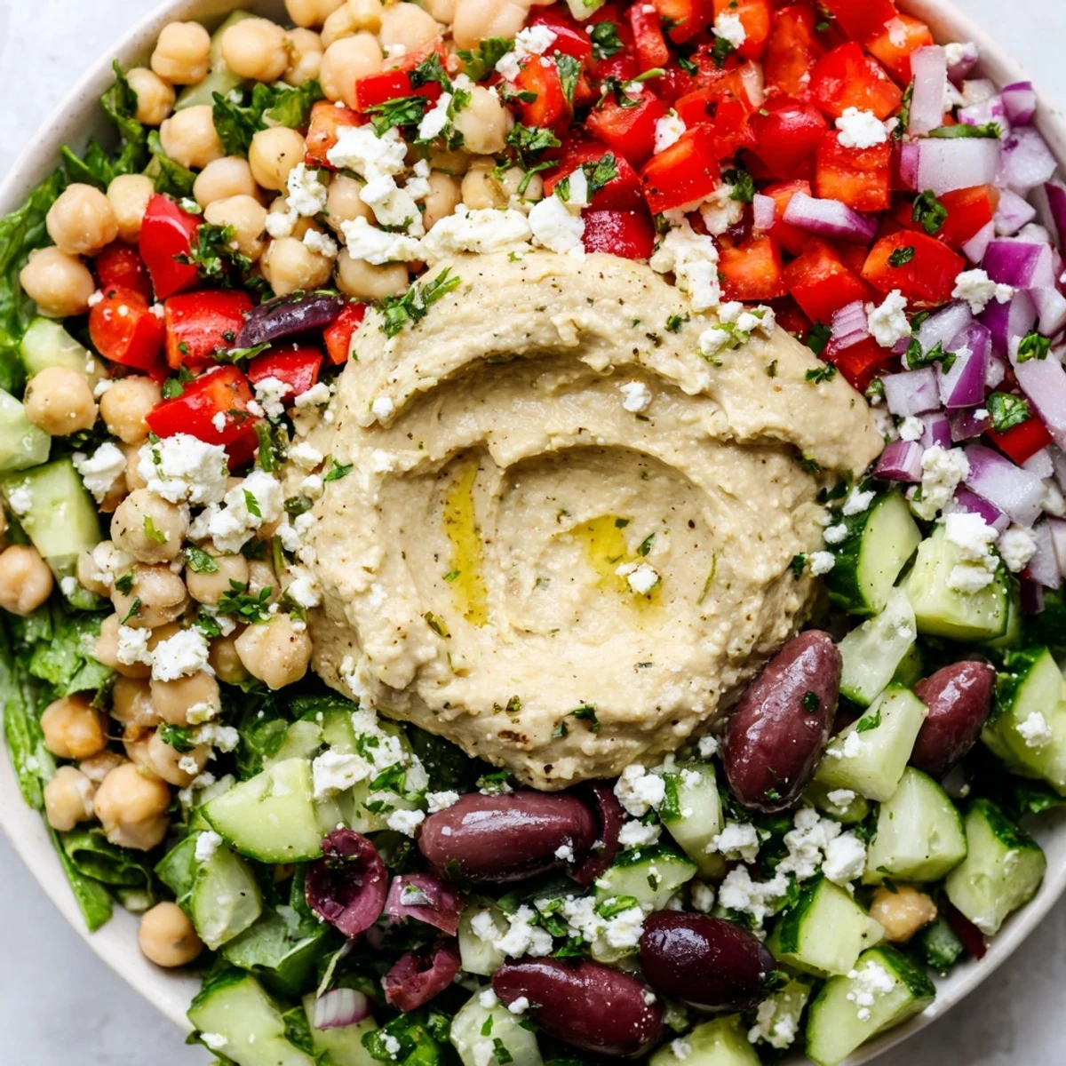 A vibrant Mediterranean Salad with Hummus topped with creamy hummus, olives, feta, and fresh parsley on a rustic table.