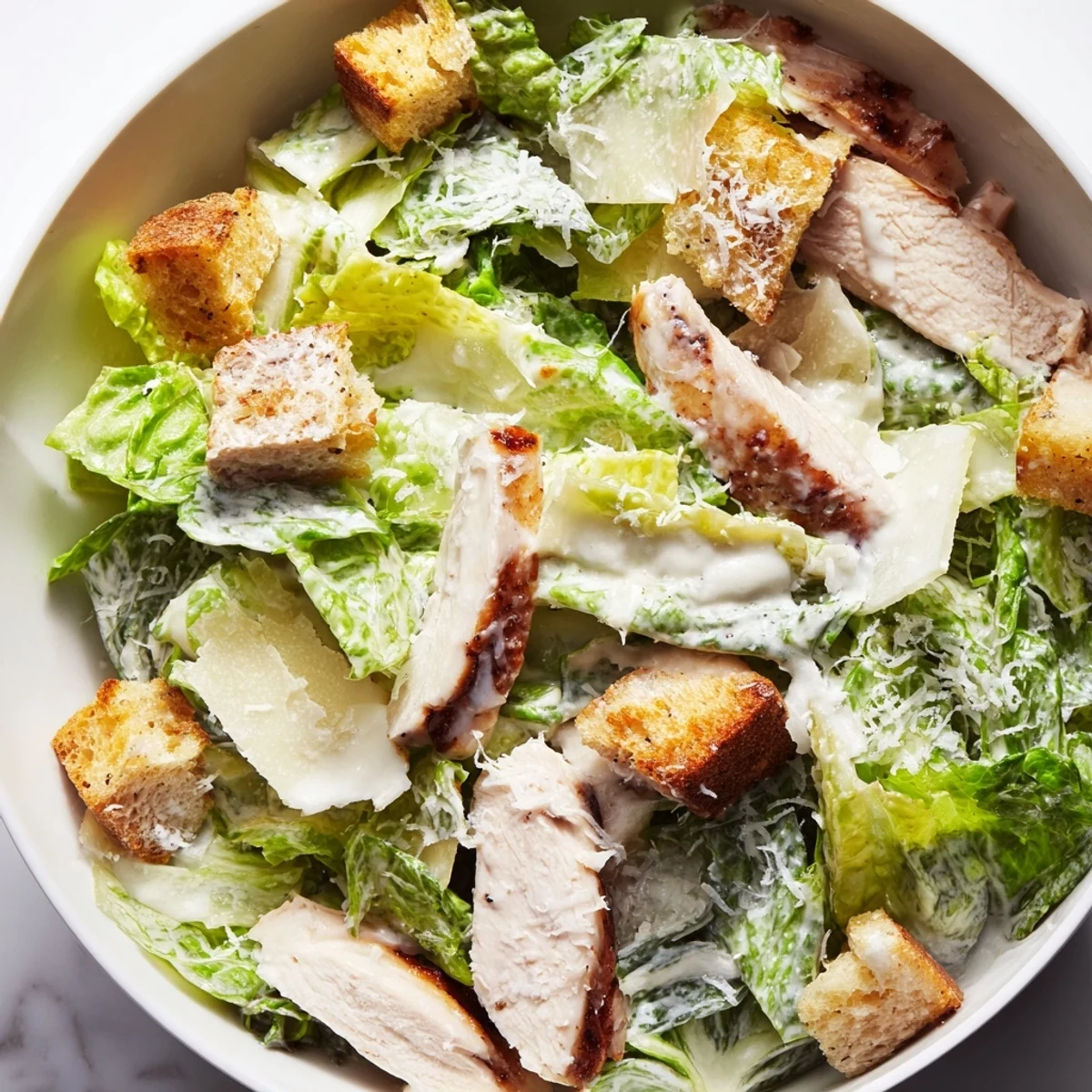 A close-up of Chicken Caesar Salad features juicy grilled chicken, crunchy homemade croutons, and shaved Parmesan on fresh greens.