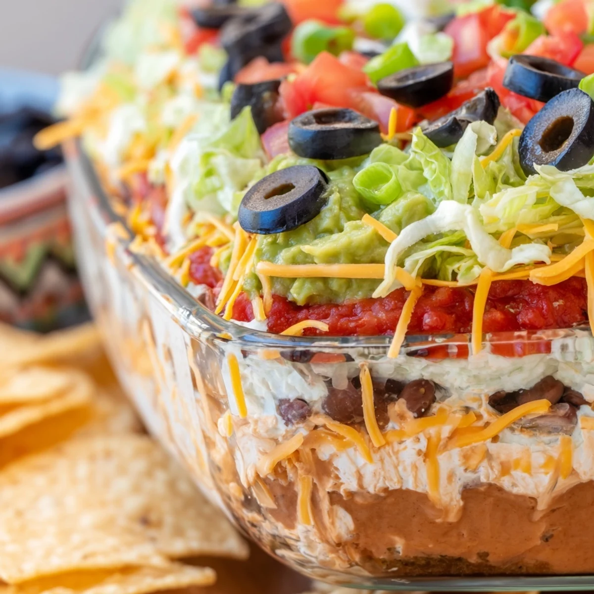 A chilled seven layer taco dip is served with crispy tortilla chips for a festive game day appetizer.