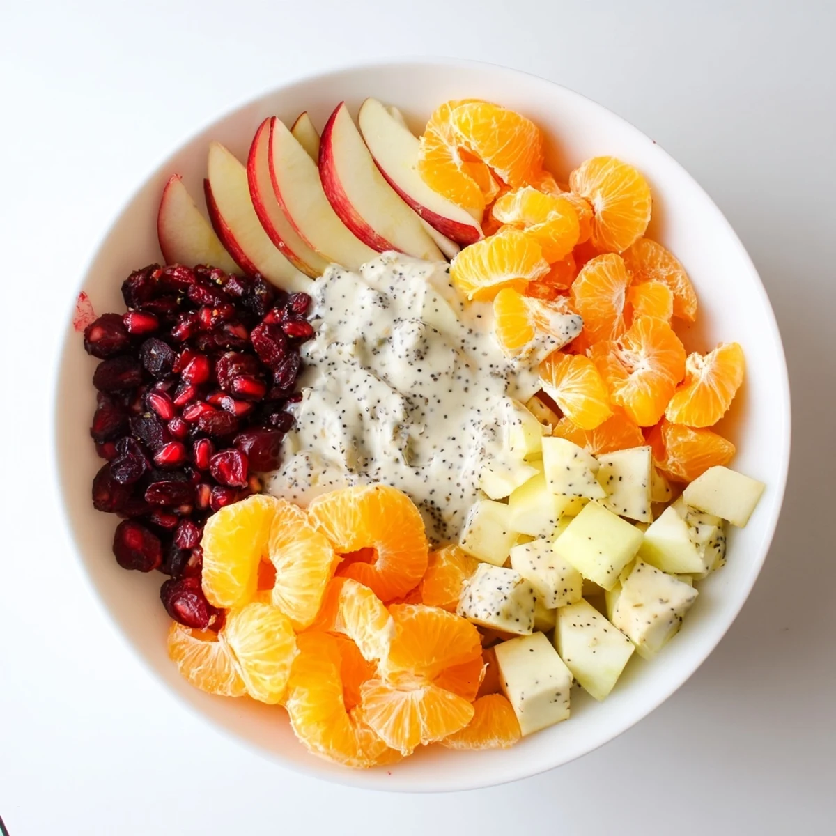 A vibrant bowl of Winter Fruit Salad with Poppy Seed Dressing, showcasing bright orange segments, apple chunks, and glistening pomegranate seeds.