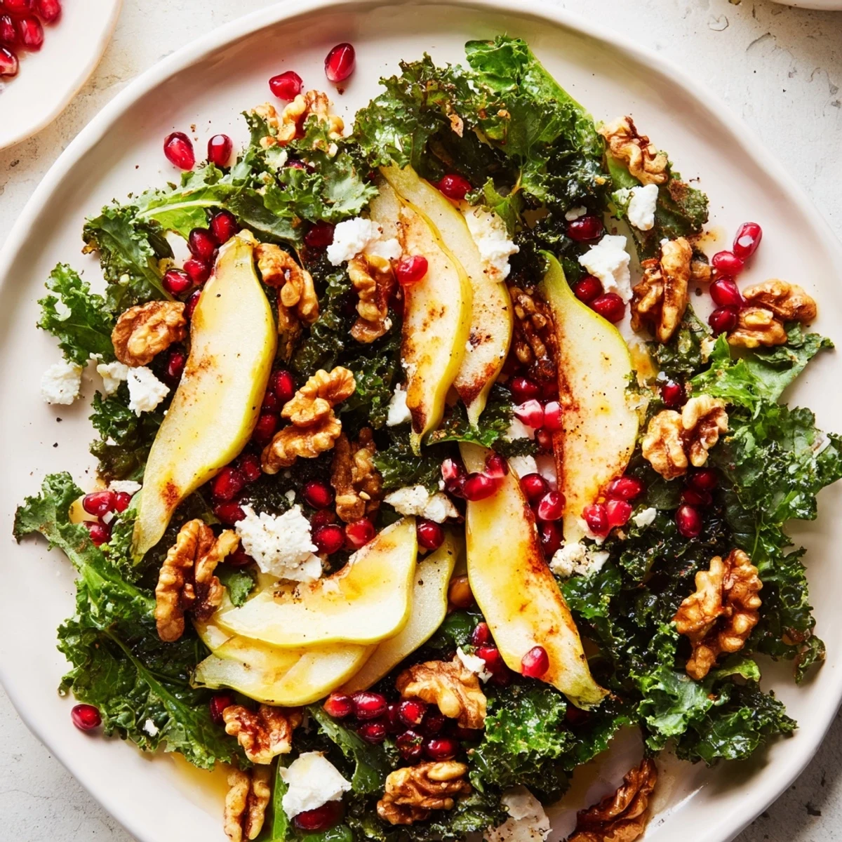 Festive Winter Green Salad with Pear and Walnuts is garnished with pomegranate seeds and crumbled goat cheese on a rustic table.