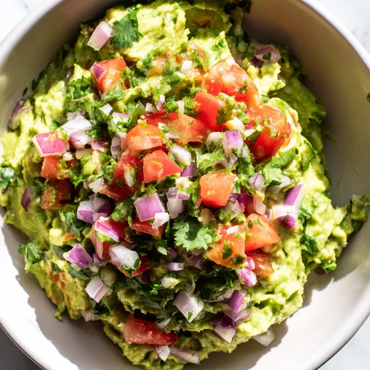 A vibrant bowl of Super Bowl Guacamole with Pico de Gallo, featuring creamy avocado chunks topped with fresh red tomato salsa and cilantro.