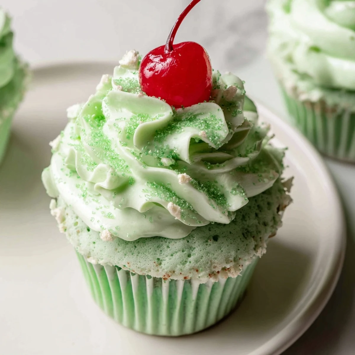 Six green-frosted Shamrock Shake Cupcakes with mint frosting, each garnished with a bright red maraschino cherry.