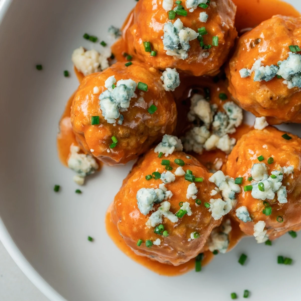 Platter of tender Buffalo Chicken Meatballs coated in vibrant orange sauce, accompanied by crisp celery and carrot sticks for a classic party appetizer.
