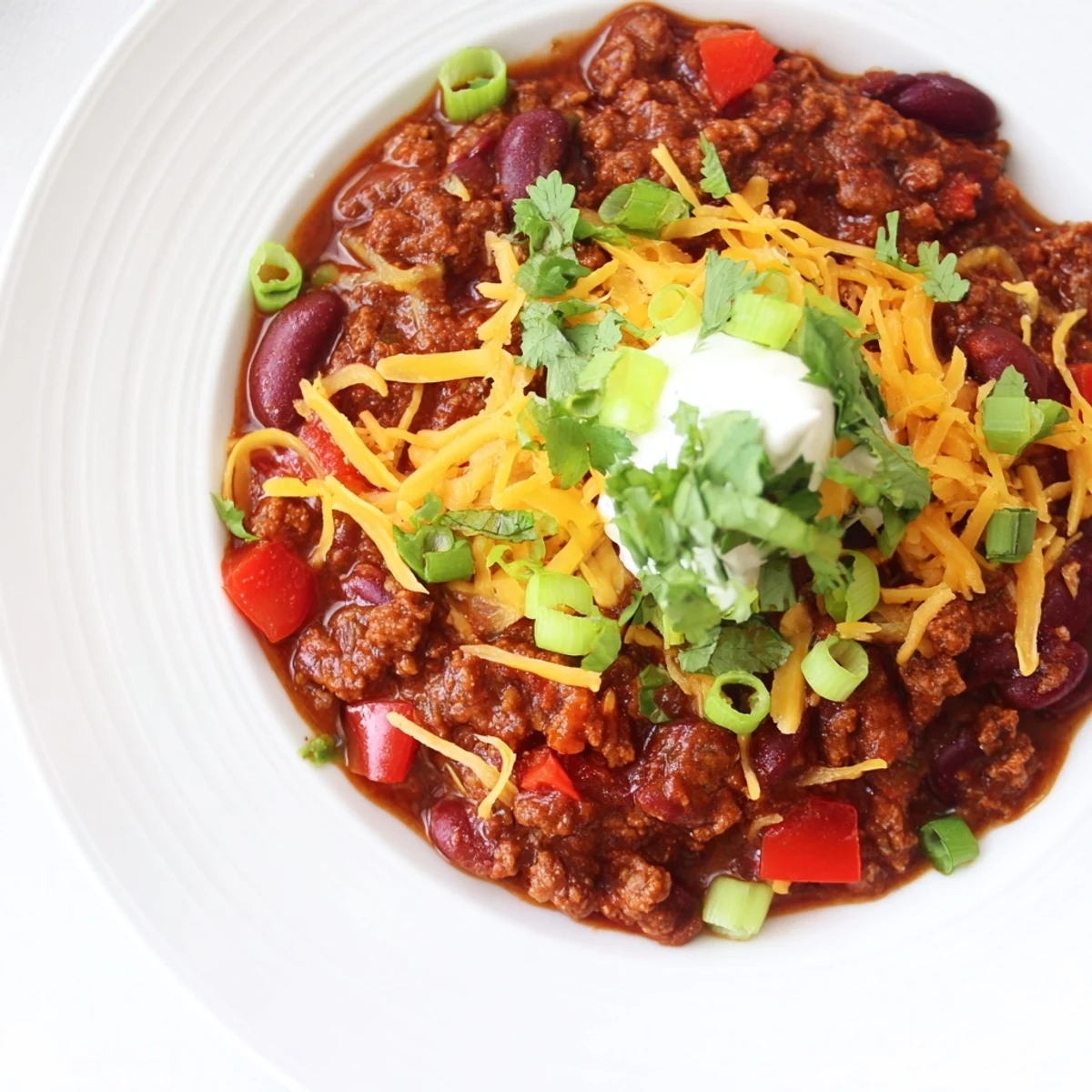 A steaming bowl of Beef Chili with Kidney Beans, garnished with sour cream and cheese, served beside warm cornbread.