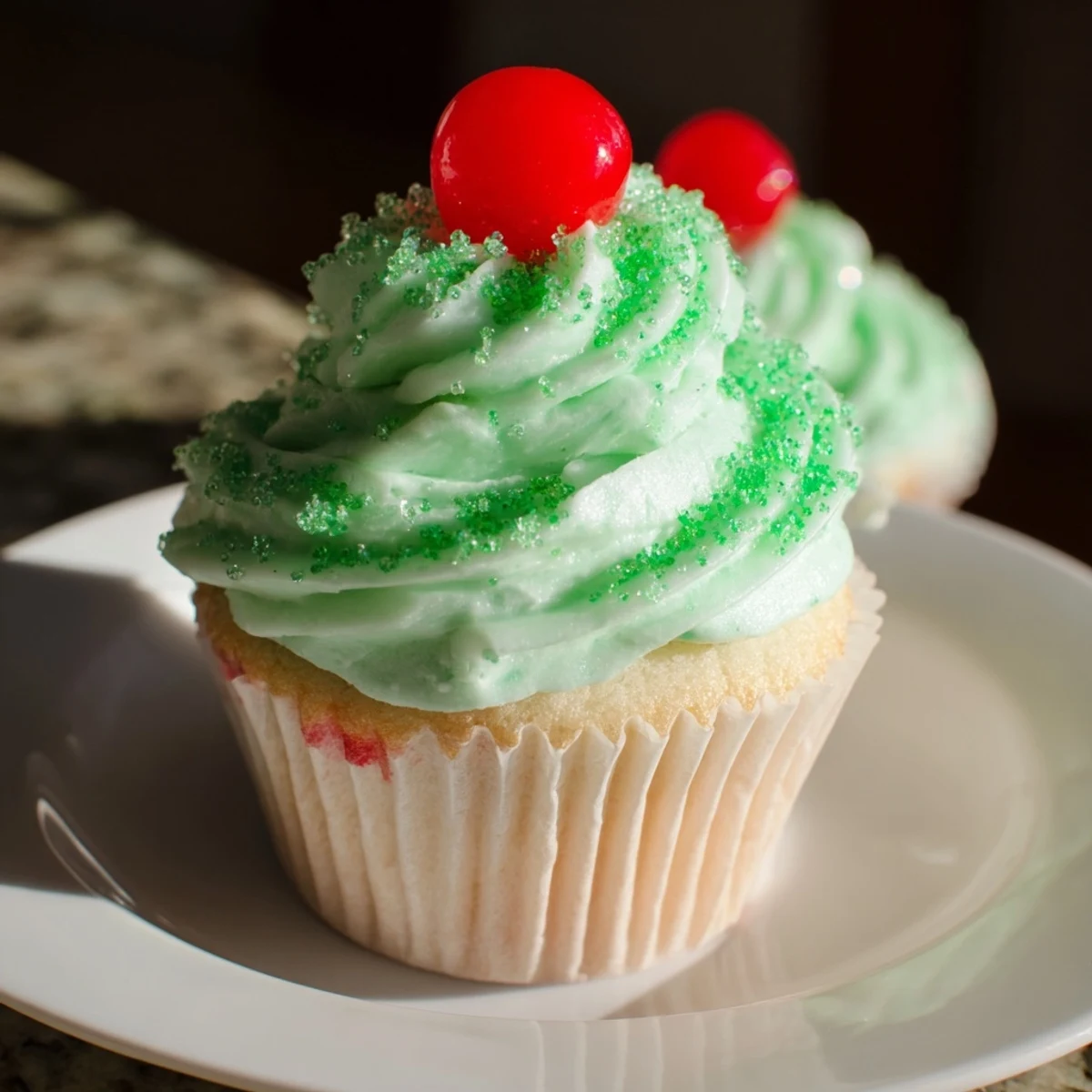 A close-up of a Shamrock Shake Cupcake reveals creamy mint frosting piped high, topped with a maraschino cherry and mini straw.  