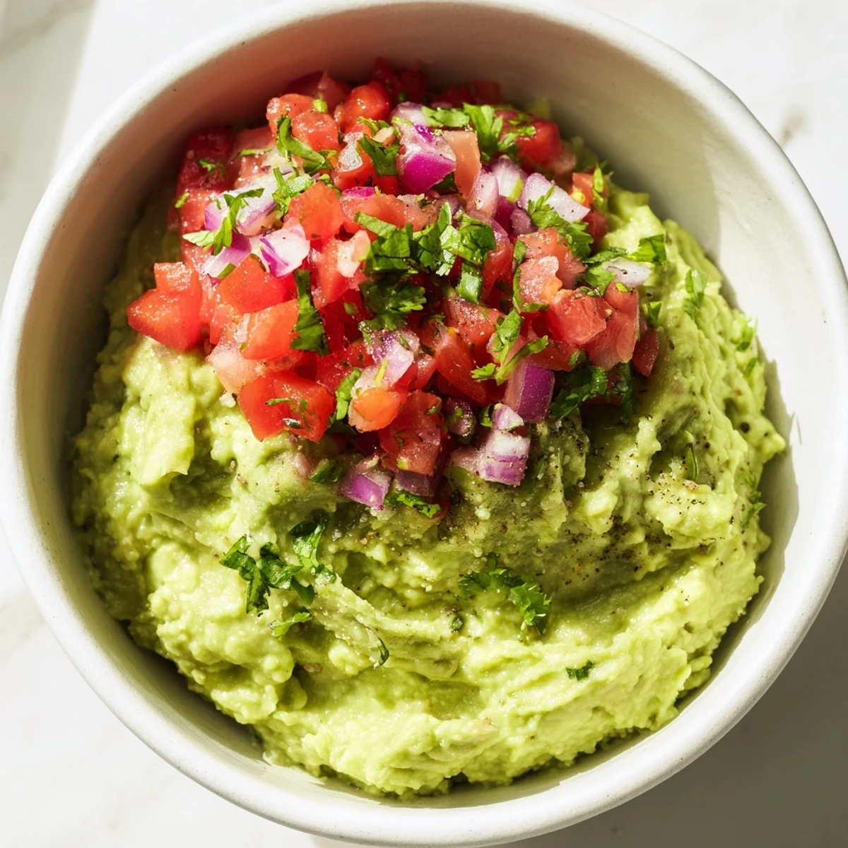 Homemade guacamole with chunky pico de gallo sits beside colorful vegetable sticks, making a refreshing and healthy party appetizer.