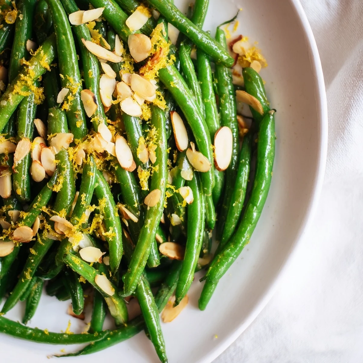 Crisp-tender green beans topped with golden toasted almonds and bright lemon zest, served as a vibrant vegetarian side dish.