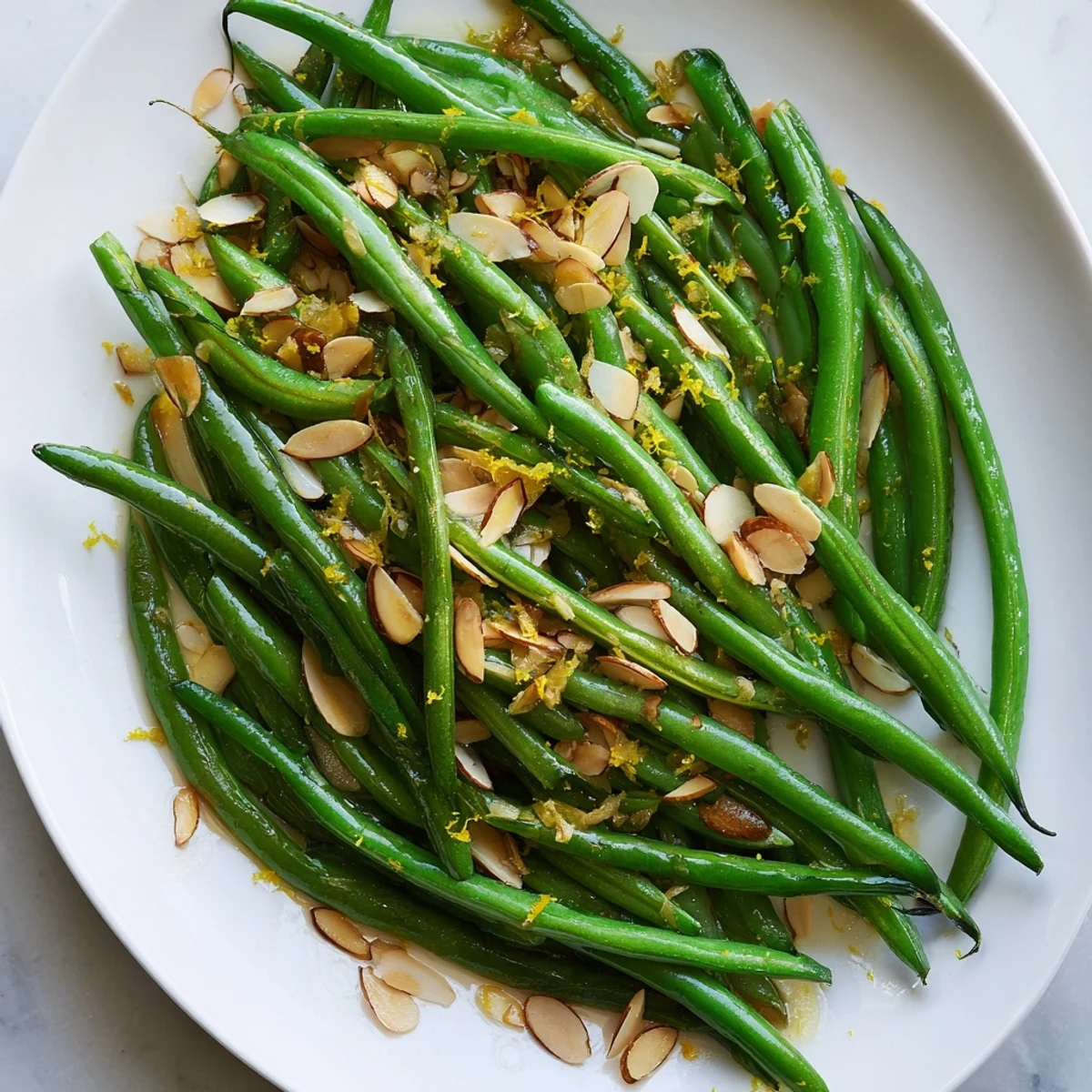 A close-up of green beans with toasted almonds and lemon zest, garnished with olive oil, ready to serve as a gluten-free side.