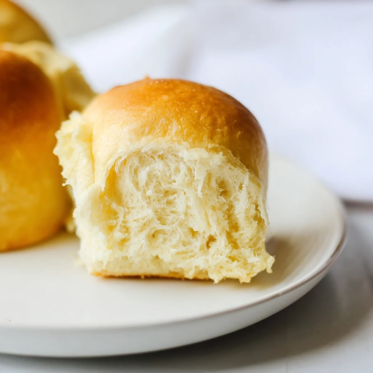 A close-up of fluffy, soft Best Vegan Dinner Rolls in a baking dish, with a golden crust and tender crumb visible.