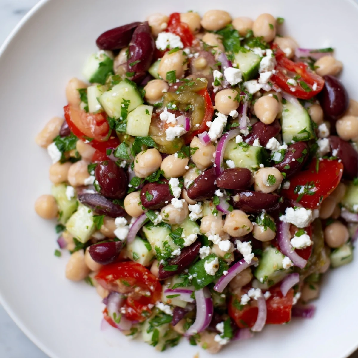 Mediterranean Dense Bean Salad served in a glass dish, showing colorful cherry tomatoes, cucumber, and fresh parsley with a lemony dressing.