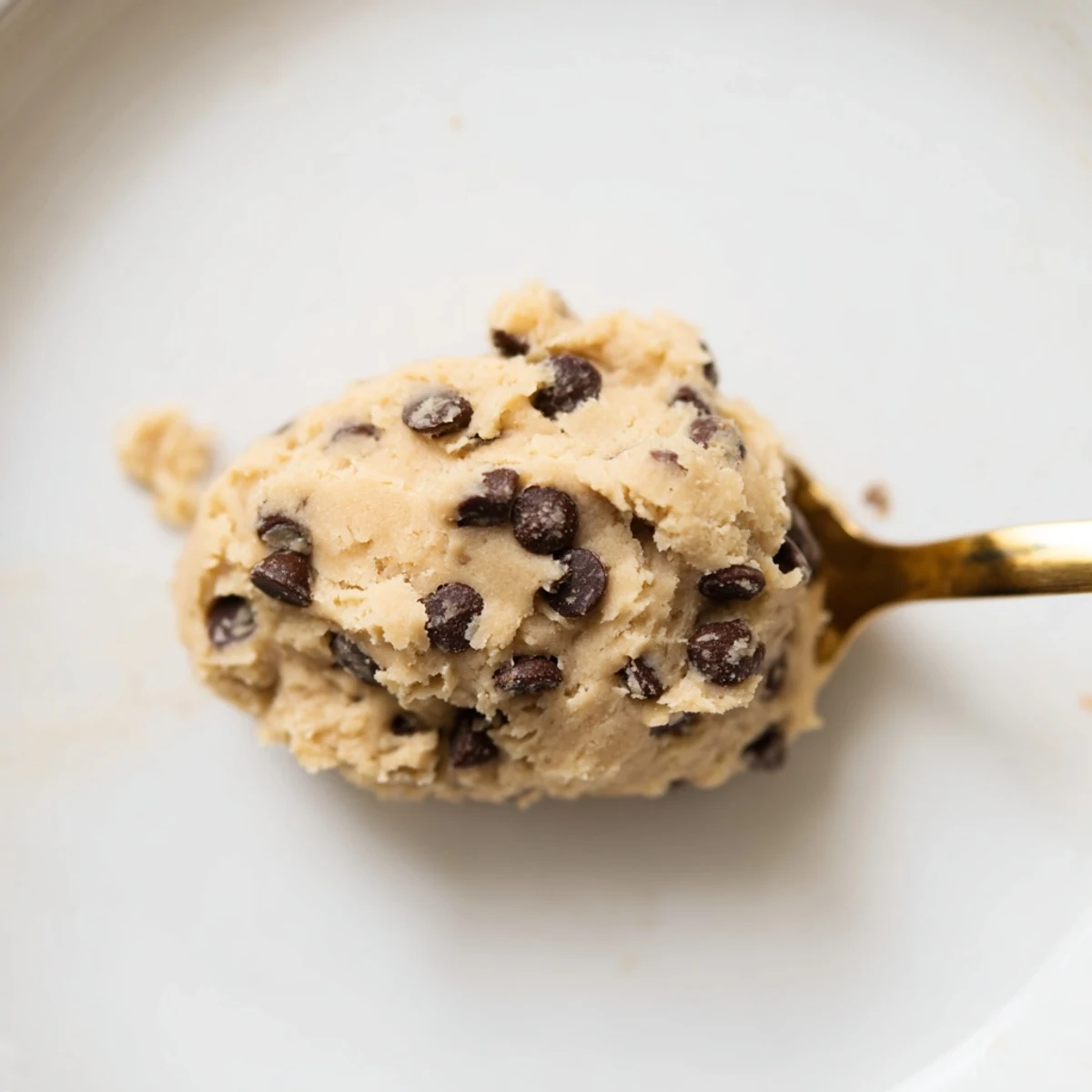 A close-up of edible Chocolate Chip Greek Yogurt Cookie Dough with mini chocolate chips on a marble surface.