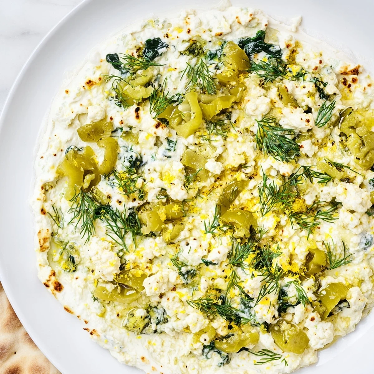 Hot and tangy Spinach and Pepperoncini Baked Feta Dip, packed with vibrant spinach and zesty pepperoncini slices, garnished with fresh herbs on top.