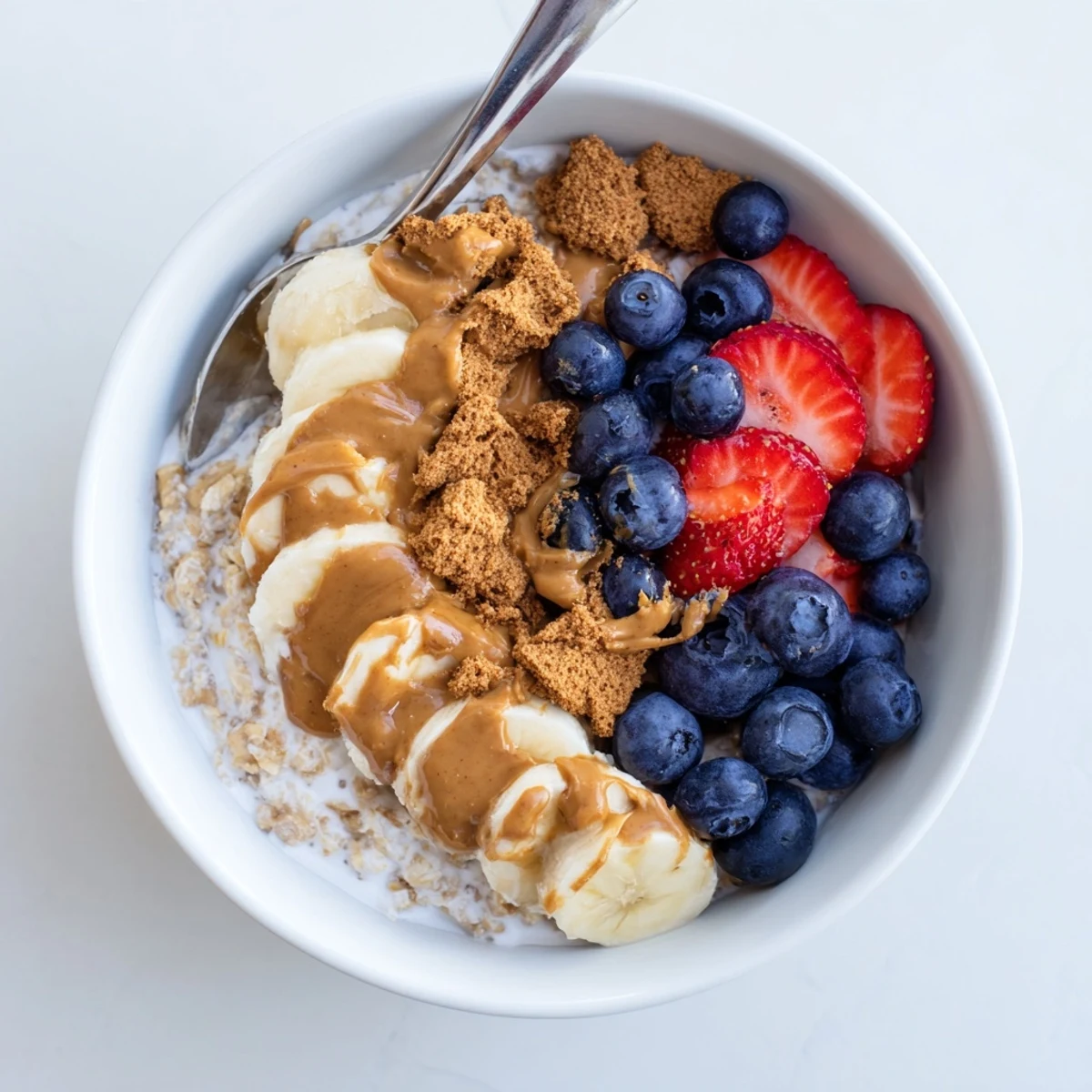 Creamy Quick Biscoff Overnight Oats layered in a jar with crushed cookies and sliced banana for a sweet breakfast.