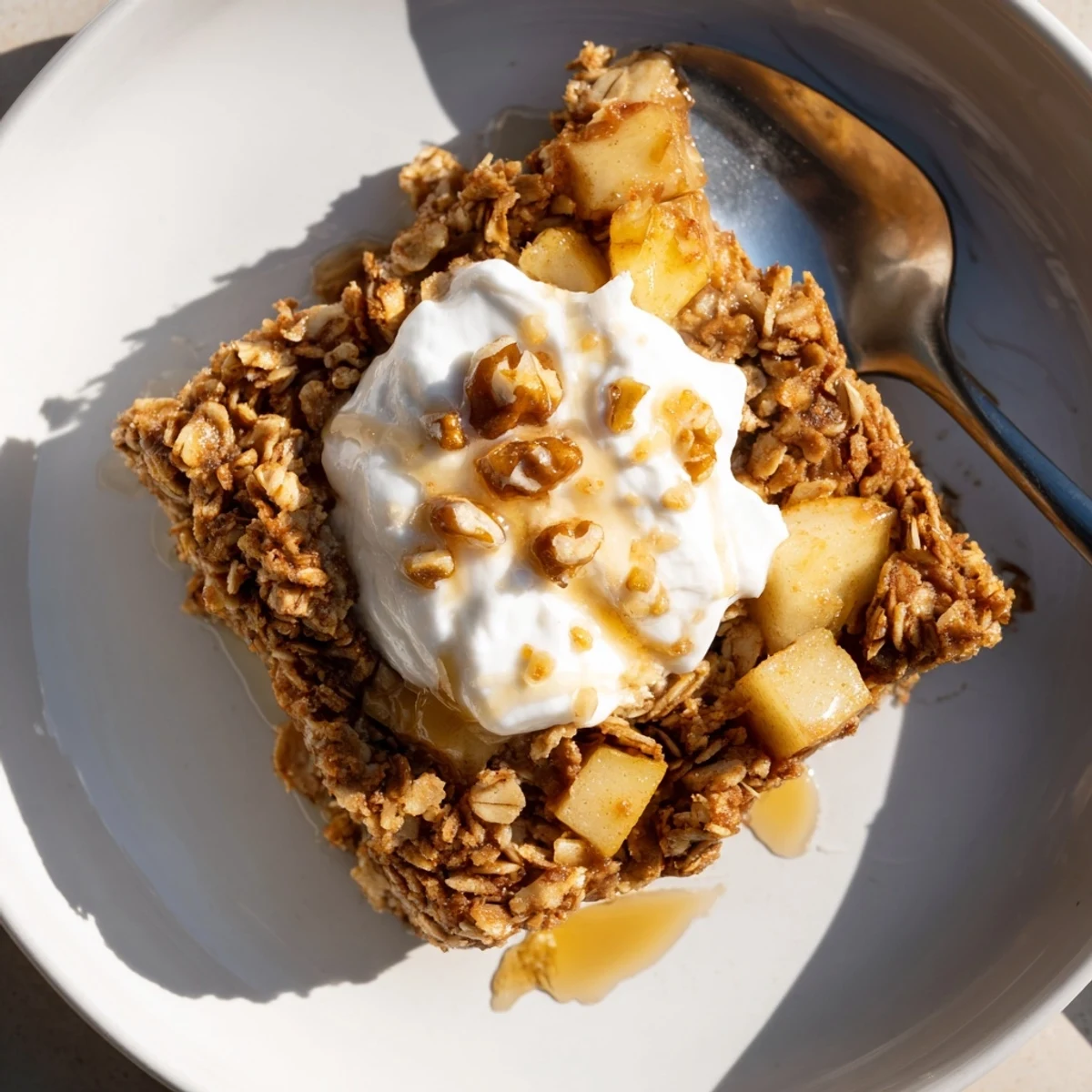 A square of baked apple oatmeal with Greek yogurt topped with creamy dollops and chopped nuts.