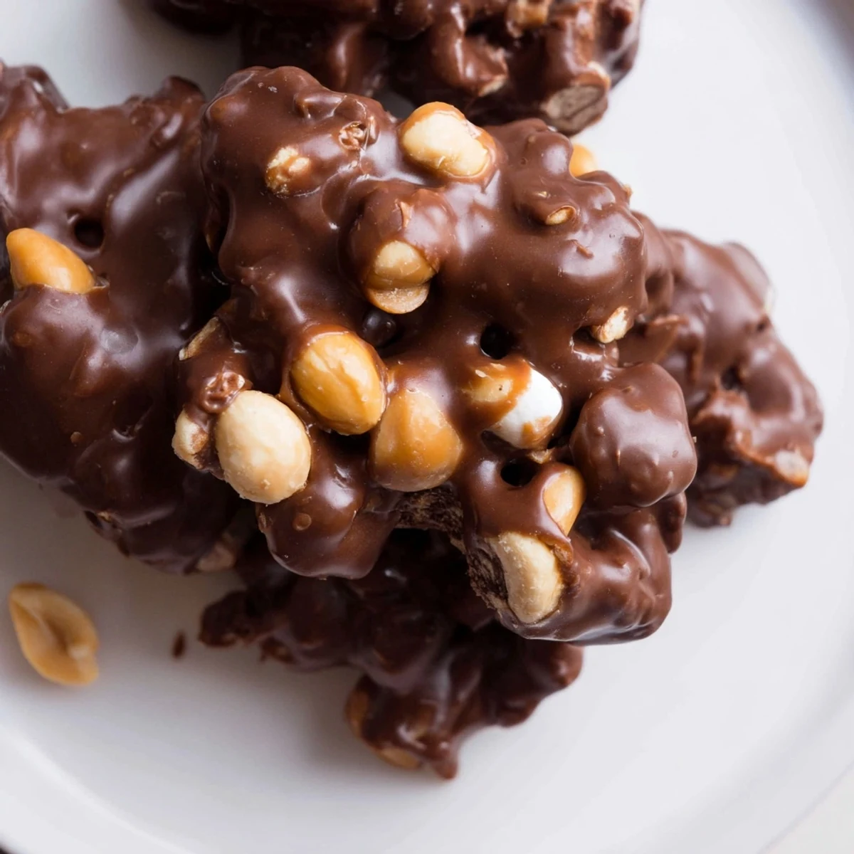 Close-up of Peanut Marshmallow Clusters on a parchment-lined baking sheet, showing glossy melted chocolate coating crunchy peanuts and soft mini marshmallows for a sweet and salty snack.