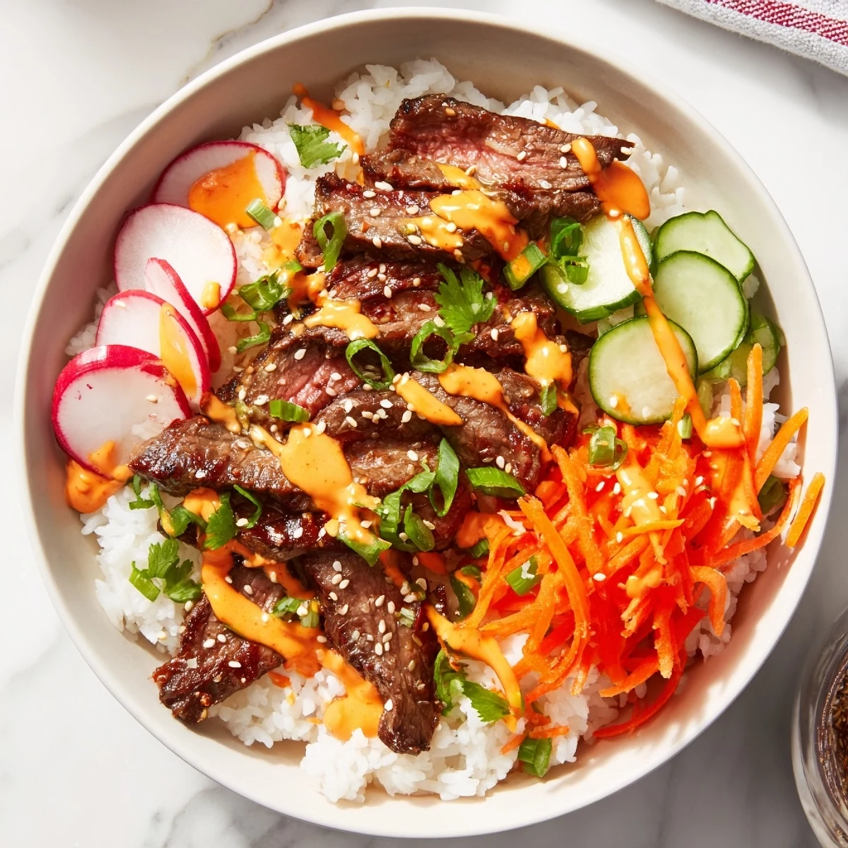 A close-up of Irresistibly Easy Korean BBQ Steak Rice Bowls with Spicy Cream Sauce, showing tender marinated steak slices over fluffy white rice, topped with crisp shredded carrots and sliced cucumbers, drizzled with a creamy red sauce.