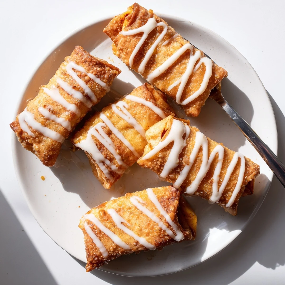 Golden, crispy Peach Cobbler Egg Rolls are displayed on a plate with a drizzled vanilla glaze.
