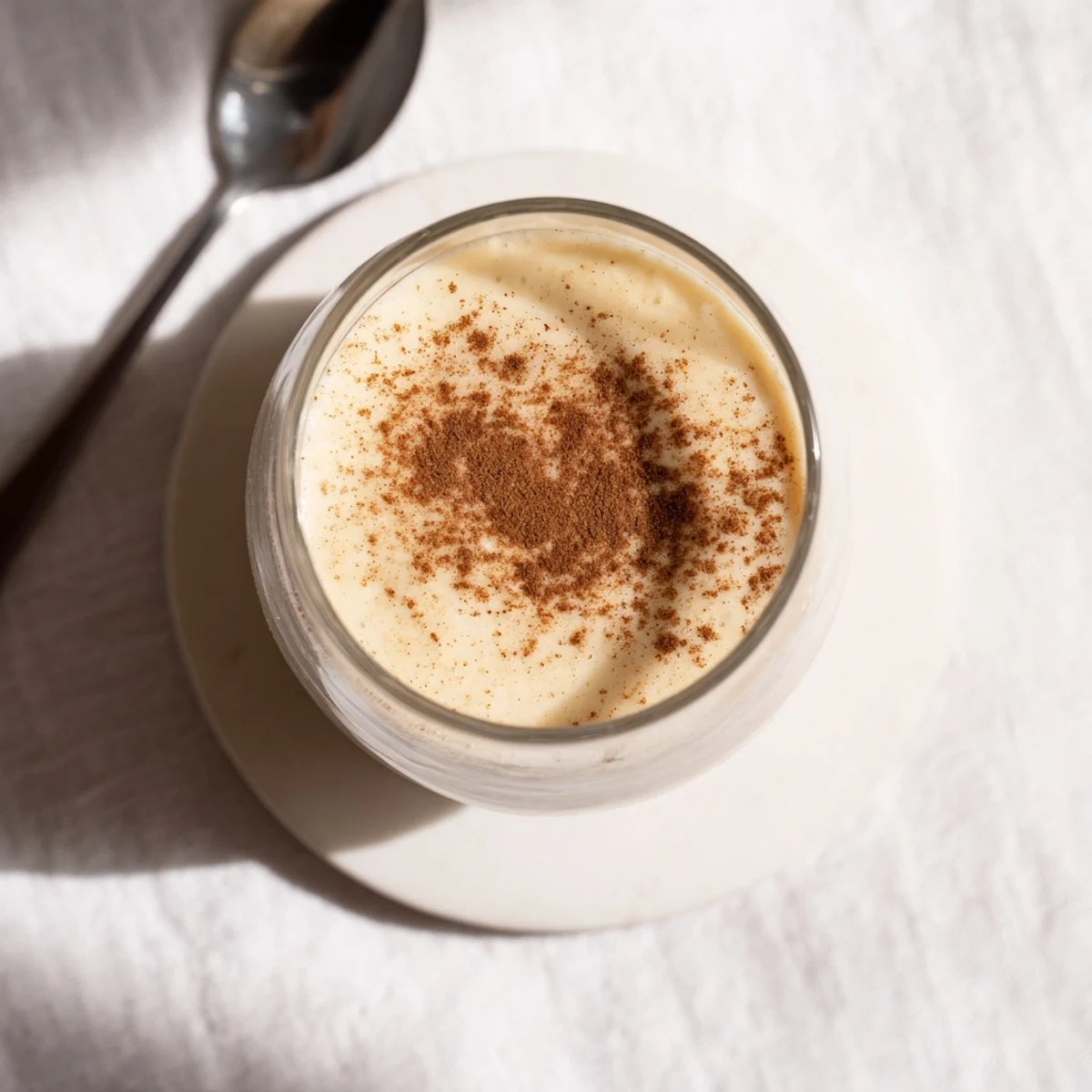 Protein-packed Greek yogurt banana smoothie in clear glass showing smooth pale yellow texture with straw garnish