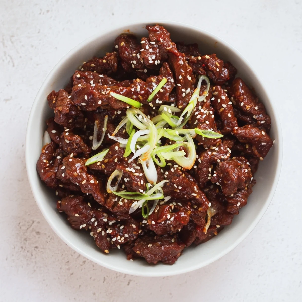 Tender slow cooker Korean beef shredded in rich dark glossy sauce garnished with green onions and sesame seeds