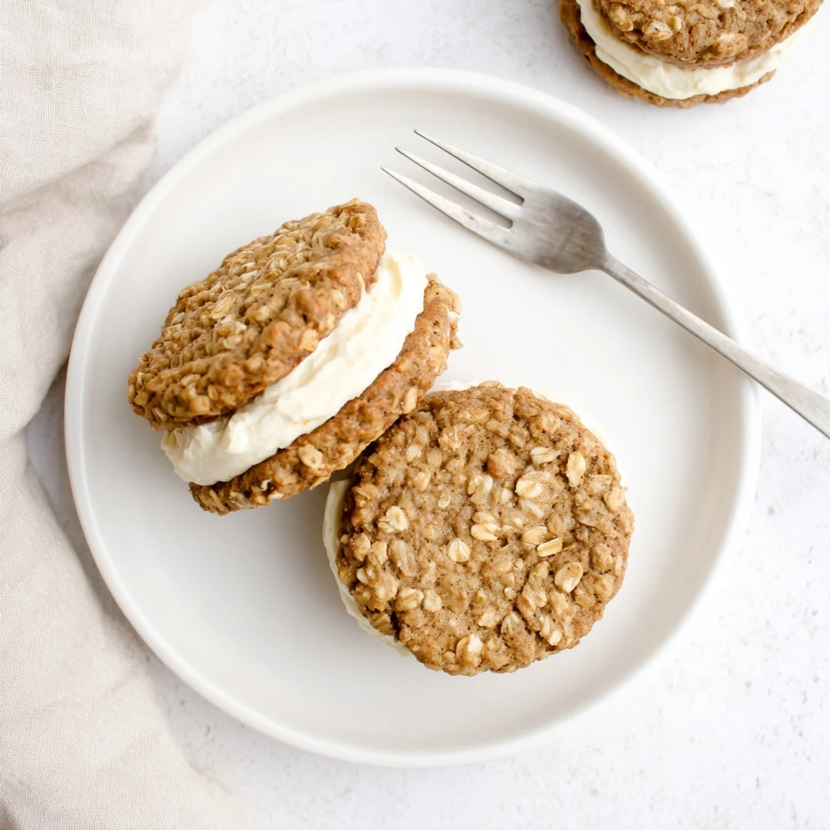 Two soft homemade oatmeal cream pies with generous vanilla frosting stacked on a white plate