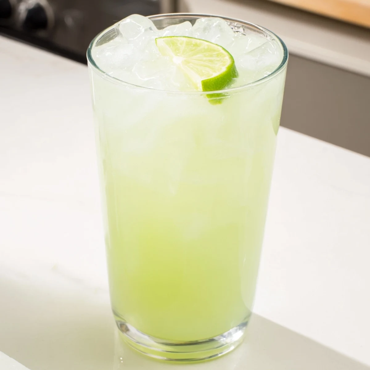Creamy Brazilian lemonade poured over ice in a tall glass with fresh lime wedge garnish