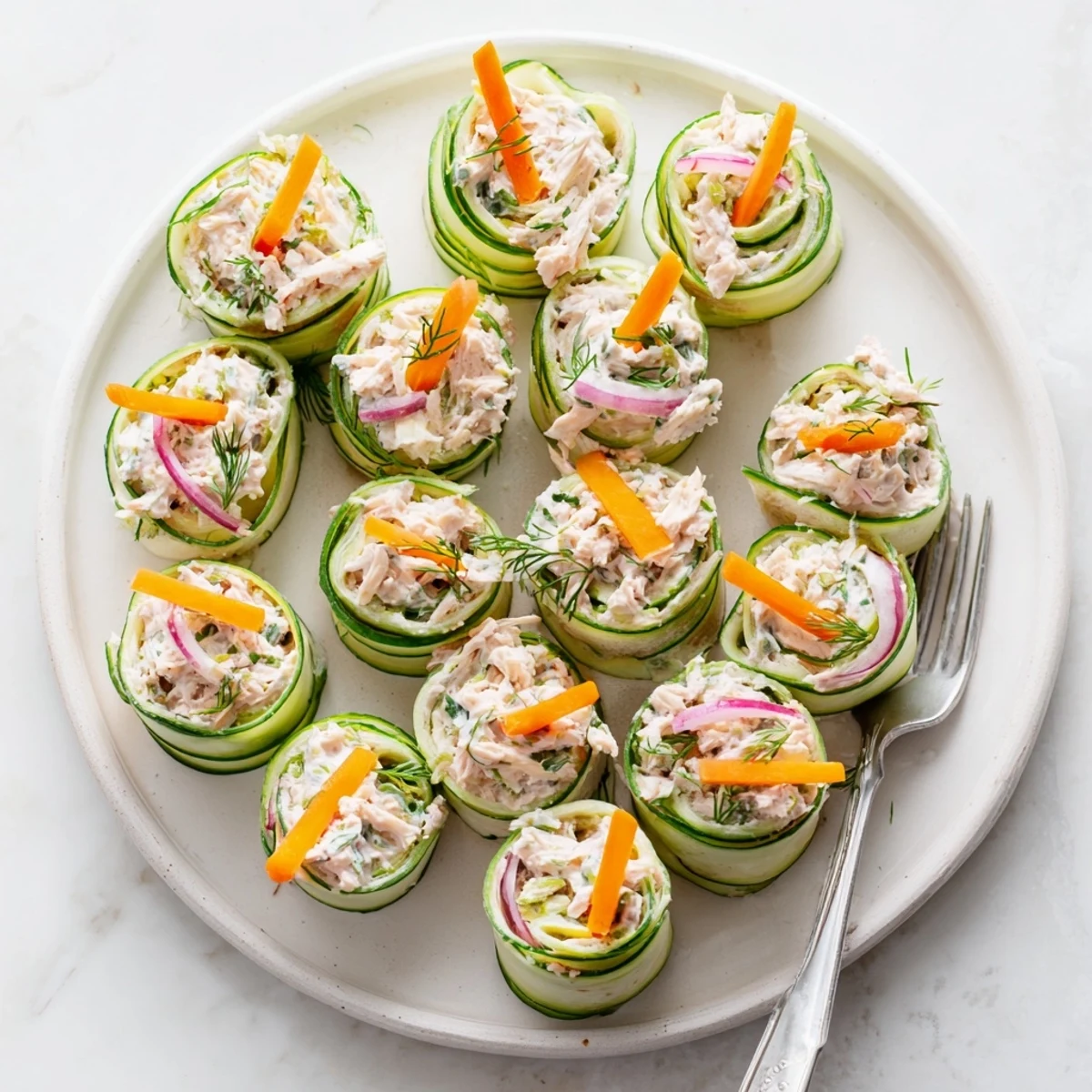 Creamy chicken salad cucumber roll ups served on a white platter with fresh herbs and julienne carrots