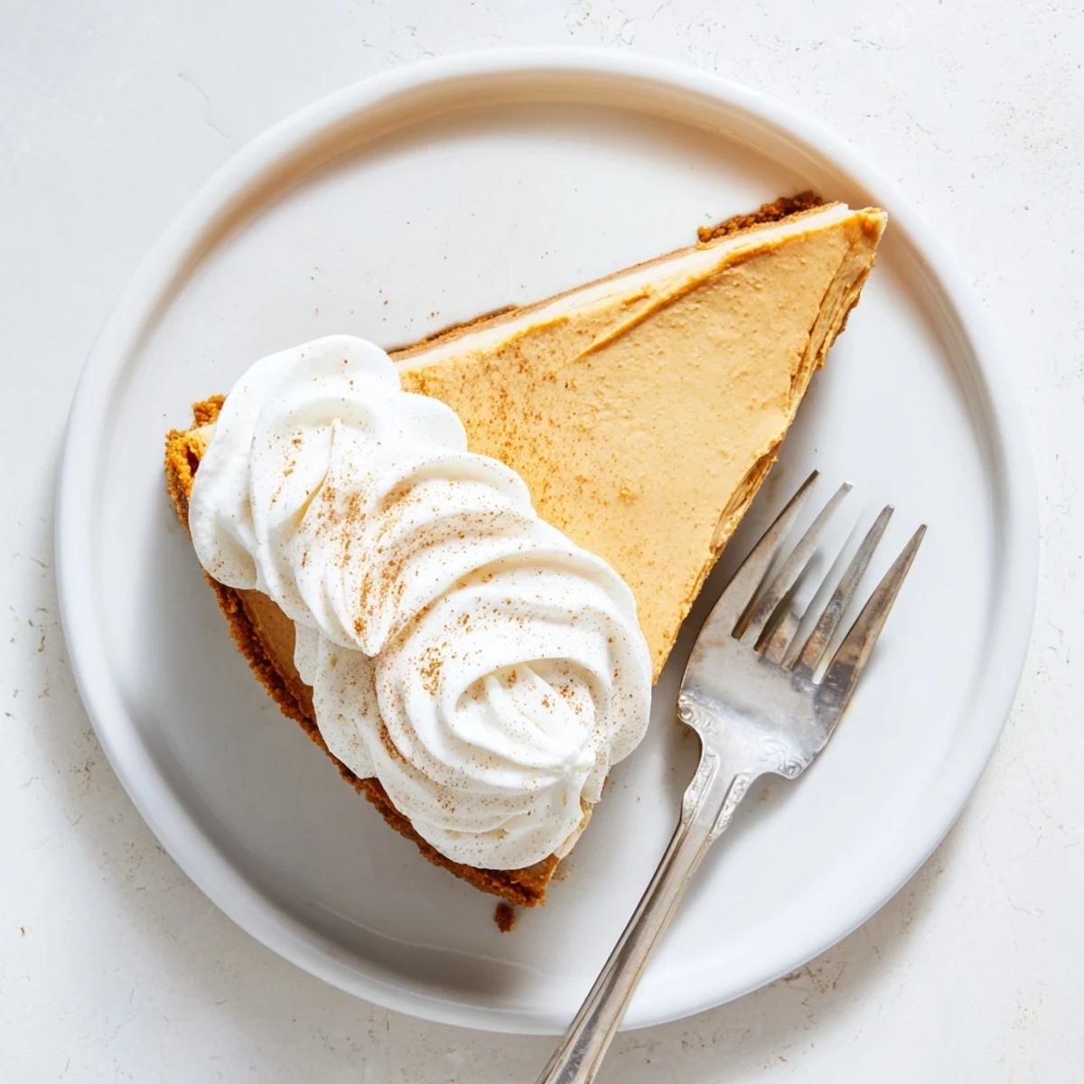 Creamy pumpkin spice Christmas cheesecake slice showing the graham cracker crust and fluffy cinnamon-dusted topping