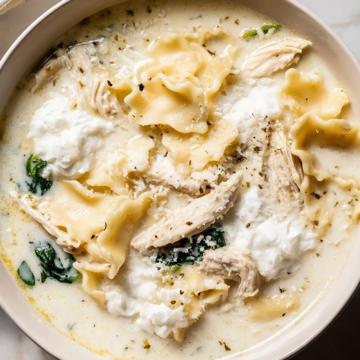 Creamy white lasagna soup with tender noodles and melted cheese in a white bowl