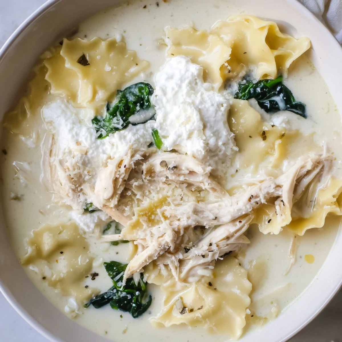 Steaming bowl of white lasagna soup topped with parmesan and fresh cracked pepper