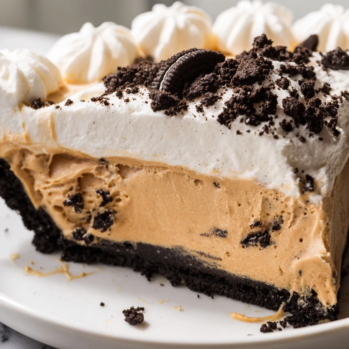 Creamy peanut butter Oreo pie sliced and topped with whipped cream and cookie crumbles