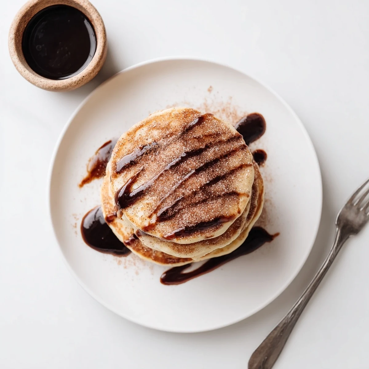 Stack of Spanish Churro Pancakes drizzled with rich dark chocolate sauce on white plate