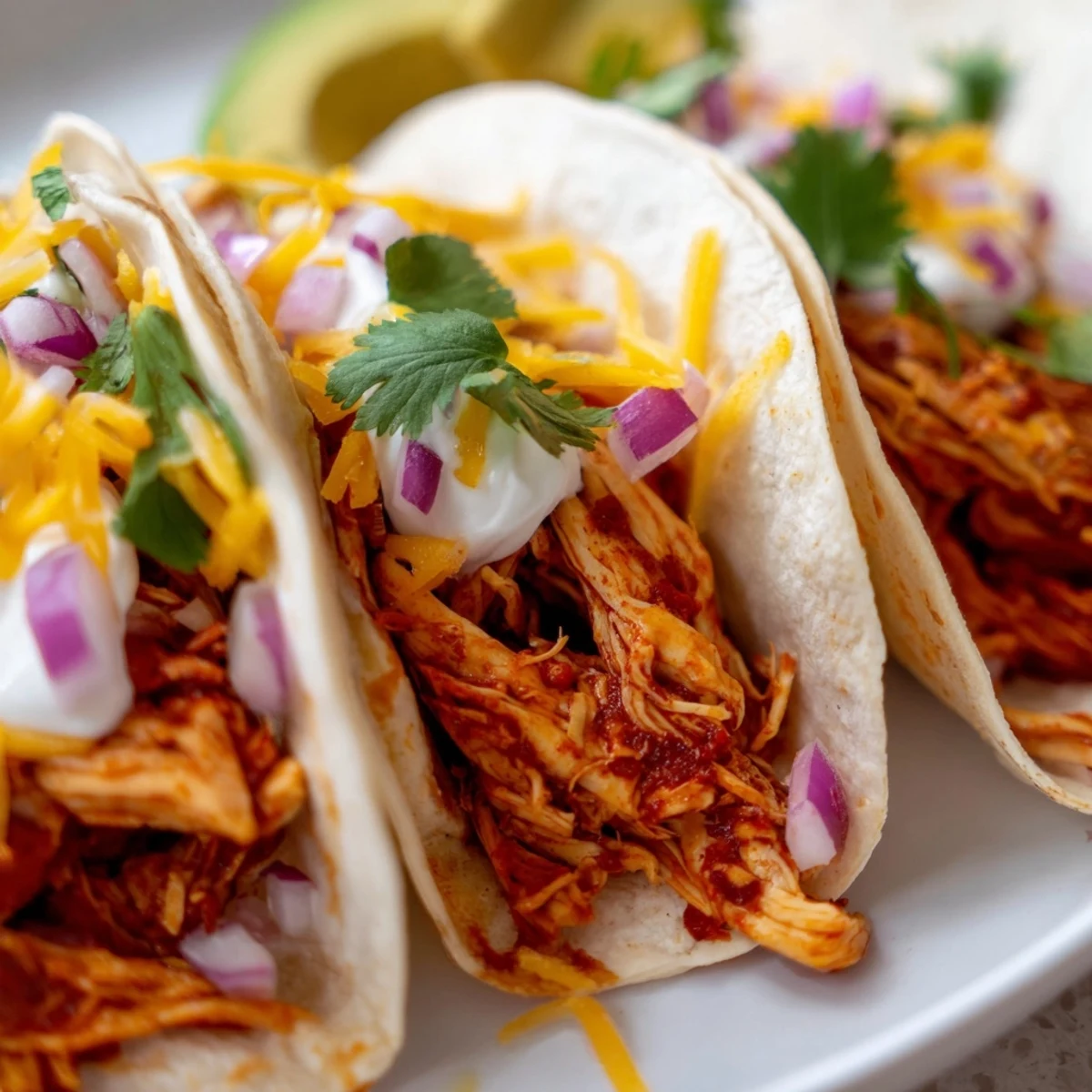 Tender slow cooker shredded chicken tacos topped with creamy avocado and zesty lime wedges