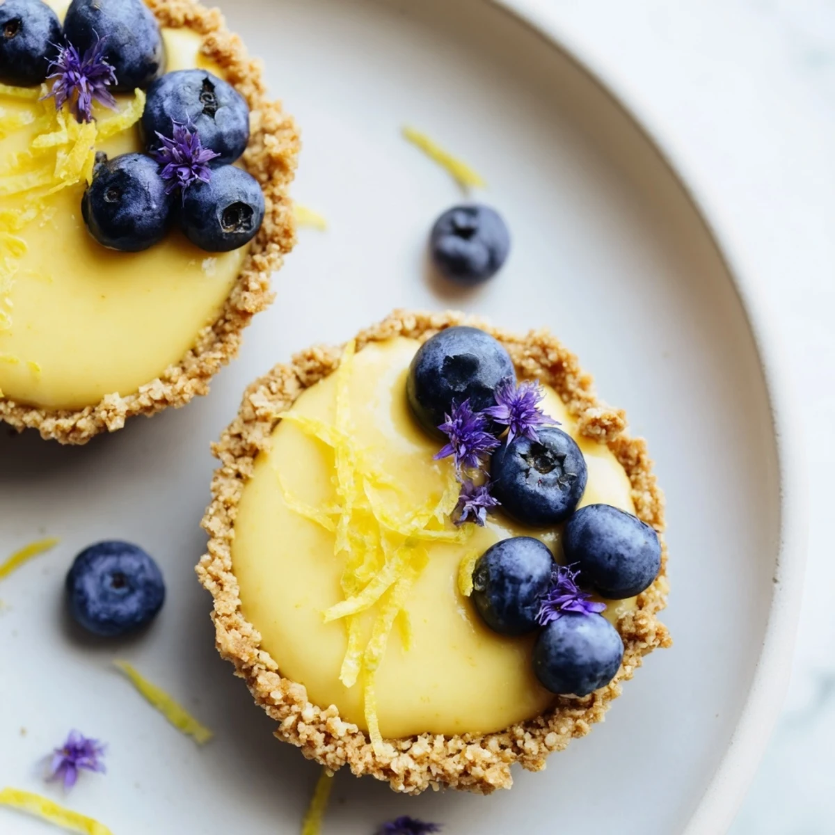 Golden mini vegan lemon tarts topped with fresh berries on a rustic white serving board