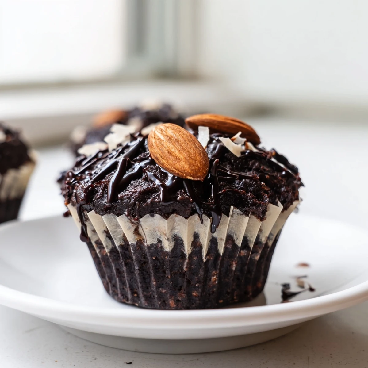 Fudgy flourless almond joy cupcakes dusted with cocoa and crowned with sweet coconut filling