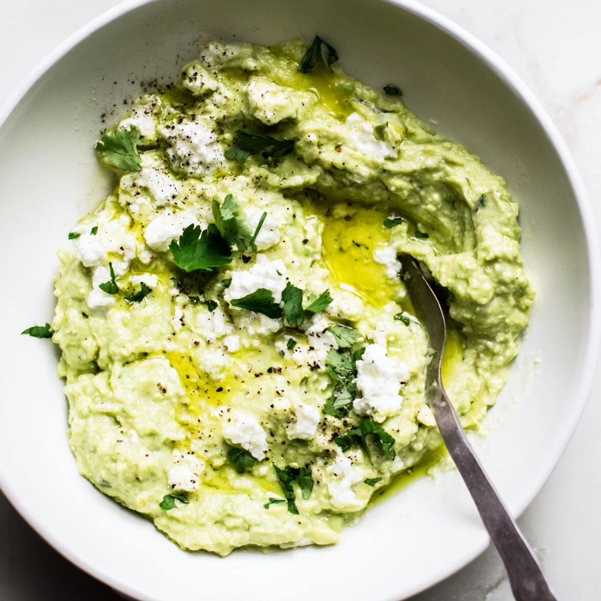 Creamy Avocado Feta Dip in bowl drizzled with olive oil, pita chips