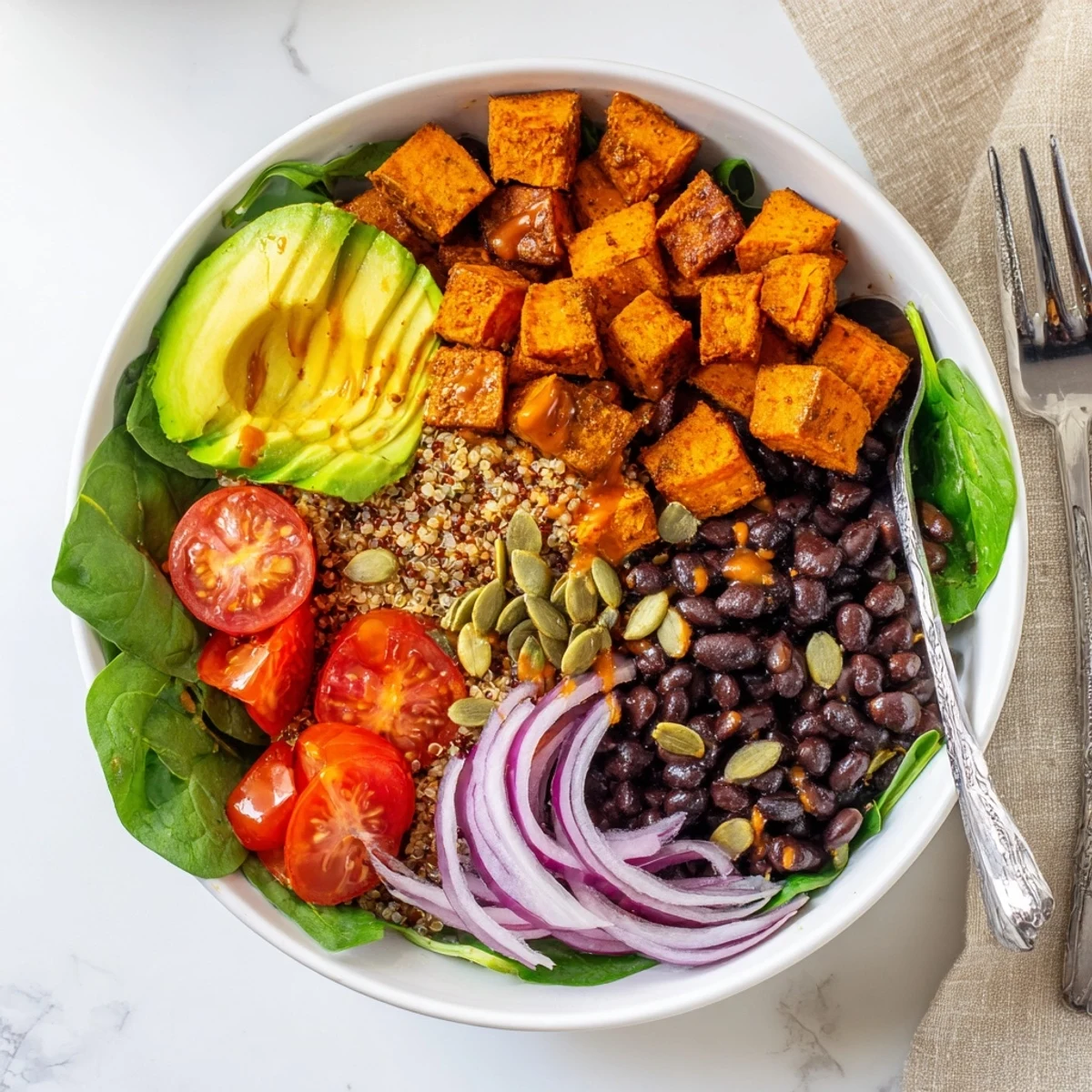 Roasted sweet potato bowl topped with black beans spinach and zesty drizzle