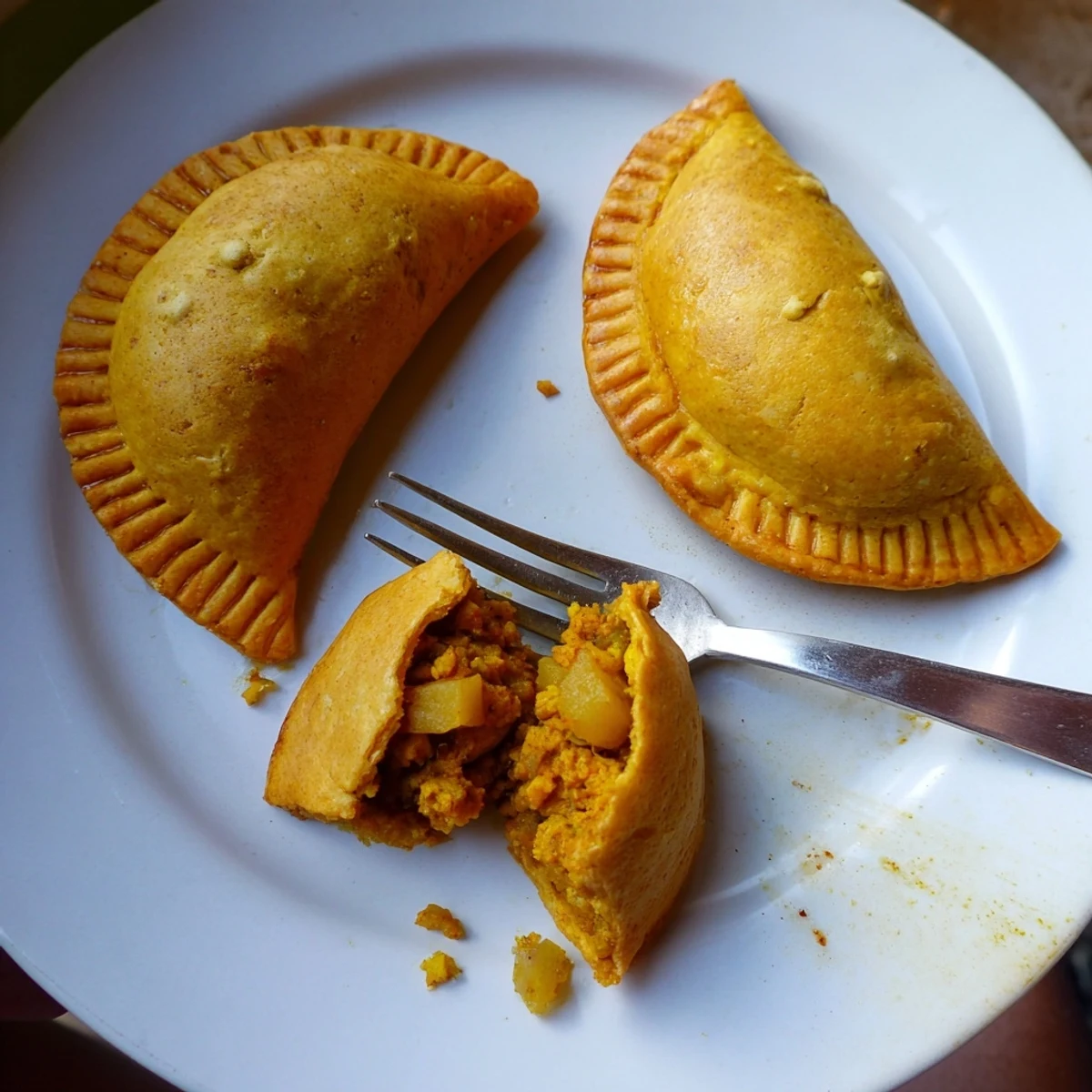 Close-up of Jamaican curry chicken patties with aromatic spiced filling oozing from crisp turmeric-yellow crust