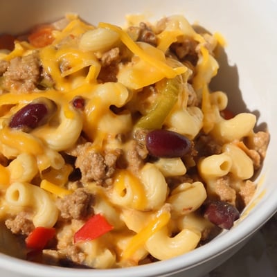 A hearty bowl of Turkey Chili Mac and Cheese is served with a side of buttery cornbread on a rustic wooden table.
