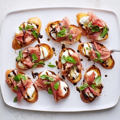 A close-up view of Mozzarella Beef Prosciutto Crostini appetizers on a wooden board, perfect for a party platter.
