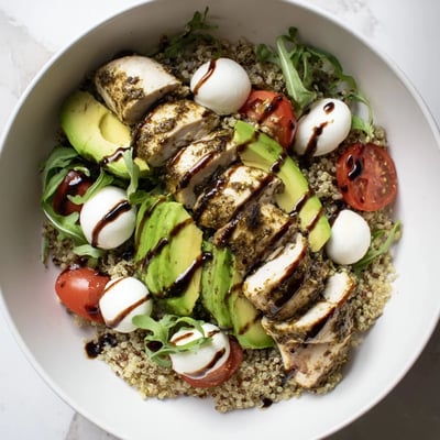 Overhead view of a wholesome Pesto Chicken Caprese Grain Bowl, showcasing golden grilled chicken slices, creamy mozzarella balls, and greens nestled in farro, ready for a healthy lunch or dinner.